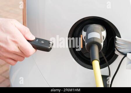 Laden eines Elektrofahrzeugs mit eingestecktem Netzkabel In und mans Hand entsperren es mit einem Schlüssel Stockfoto