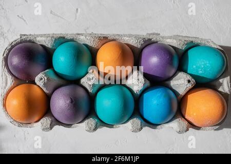 10 farbenfrohe Ostereier in blau, türkis, lila und orange in einem Eierkarton. Stockfoto