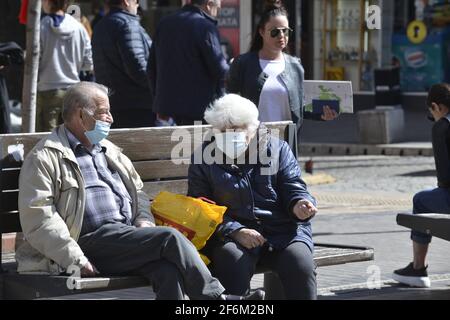 Sofia, Bulgarien - 1. April 2021: Zwei ältere Menschen sitzen auf einer Bank in Schutzmasken Stockfoto