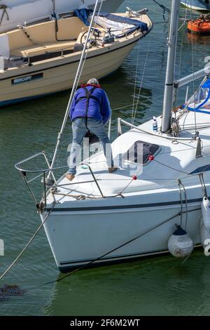 Segler, der auf dem Bug einer großen modernen Segelyacht oder eines Bootes auf einem Liegeplatz in einem Jachthafen steht Stockfoto