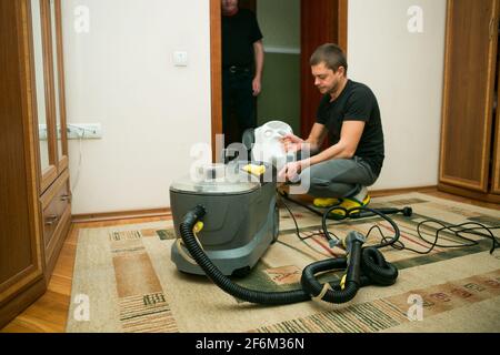 Der Prozess der Reinigung von Teppichen mit einem Dampfstaubsauger. Ein Mitarbeiter eines Reinigungsunternehmens bereitet die Geräte auf die Arbeit vor. Stockfoto