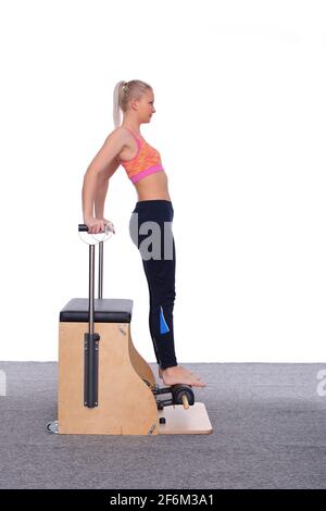 Ein 20-jähriger Trainer demonstriert, wie Pilates an einer Maschine richtig trainiert werden kann. Sie steht auf ihren Zehen und hält sich mit ihren Händen. Stockfoto