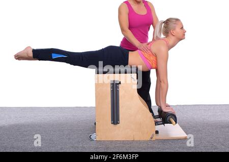 Der 50-jährige Trainer lehrt ein junges Mädchen, Pilates auf einem Fahrstuhlstuhl zu üben. Sie korrigiert und passt die Körperposition des Schülers an Stockfoto