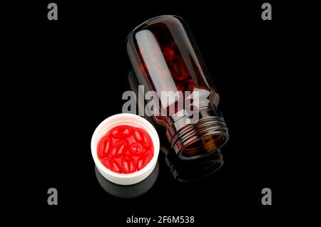 Rote Vitamintabletten im Fläschchen auf glänzendem schwarzem Hintergrund Stockfoto