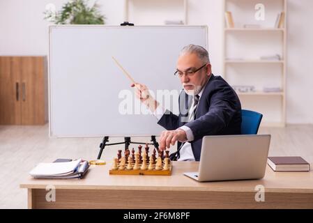 Alter Geschäftsmann Angestellter, der Schach am Arbeitsplatz spielt Stockfoto