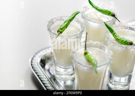 Kokosnusscocktail in einem Glas, das mit Kokosflocken und grünem Vogelauge-Chili dekoriert ist und auf einem silbernen Tablett serviert wird, mit weißen Getränken Stockfoto