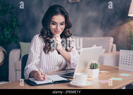 Foto von schönen optimistischen Brünette lockige Frisur Dame tragen Brillen Weißes Hemd allein zu Hause schreiben Stockfoto