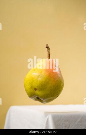 Birne schwebt in der Luft auf einem weißen Tisch und gelbem Hintergrund. Stockfoto