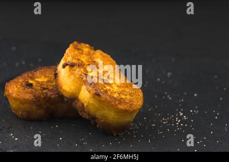Nahaufnahme einiger Torrijas mit Zimt und Zucker, ein typisches Dessert der Karwoche in Spanien auf einem schwarzen Schiefer mit Kopierfläche. Stockfoto