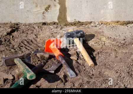 Unschärfe-Hammer, Hammer, Meißel und Bajonett der Schaufel liegen auf dem Boden. Satz von Werkzeugen für die Verlegung von Pflastersteinen. Vorbereitung Terrasse mit Stein zu legen. Stockfoto