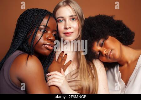 Junge hübsche kaukasische, afro, skandinavische Frau posiert fröhlich zusammen auf braunem Hintergrund, Lifestyle diverse Nationalität Menschen Konzept Stockfoto