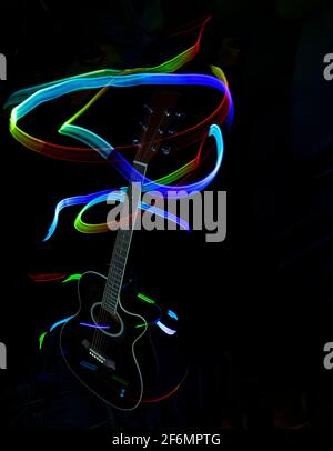 Silhouette einer akustischen Gitarre im Dunkeln beleuchtet mit Spuren von farbigem Licht, Malerei mit Licht, farbige Lichter, lange Belichtung, vertikal Stockfoto