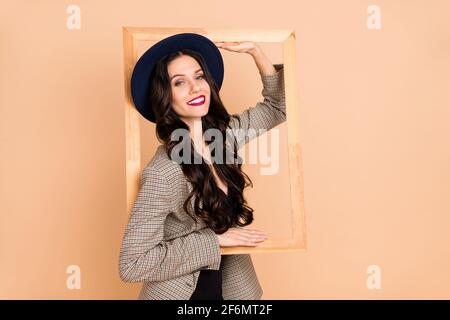 Foto von niedlichen liebenswert junge Frau tragen karierten Jacke Kopfbedeckung Innen Holzrahmen isoliert beige Farbe Hintergrund Stockfoto