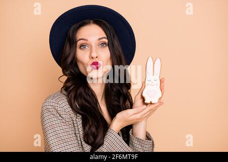 Foto Porträt einer lächelnden Frau halten osterkeks Kaninchen senden Air Kiss Pouted Lippen isoliert auf pastellfarbenen beigen Hintergrund Stockfoto