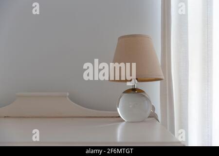 Nahaufnahme einer kleinen Lampe, die auf einem Holzdekorationstisch neben dem Vorhang steht. Stockfoto
