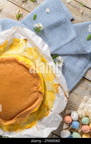 Portugiesischer Biskuitkuchen, eingewickelt in das typische Backpapier, auf Holzhintergrund mit bemaltem ostereier-Dekor. Stockfoto