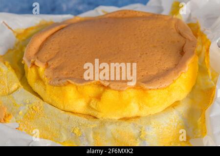 Portugiesischer Biskuitkuchen, eingewickelt in das typische Backpapier, auf Holzhintergrund mit bemaltem ostereier-Dekor. Stockfoto