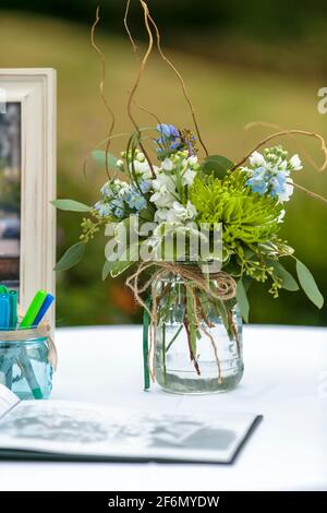 Blumen in einem Einmachglas als Dekor für ein Register Tisch bei einer Hochzeit im Freien mit einem Schild im Buch Stockfoto