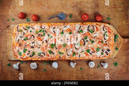 Lange Pizza mit Chiken und Pilzen liegt auf einem Holztisch. Römische Pizza auf einem Holzspatel. Eine Meter lange Pizza.auf der Pizza Holzspachtel. Stockfoto