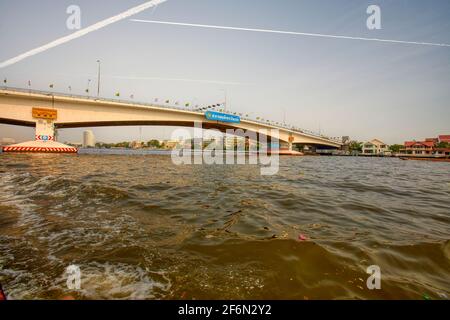 Unter der Phra Pin Klao Brücke fahren Sie mit einem Wassertaxi mit einem langen Boot, während Sie den Chao Phraya Fluss in Bangkok, Thailand, entlang fahren Stockfoto