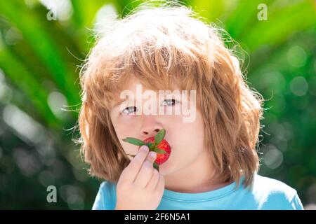 Kind, das Erdbeeren auf grünem Frühlingshintergrund isst. Stockfoto