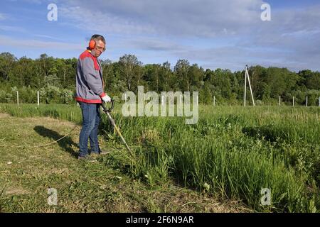 Mann mäht das Gras mit einem Trimmer, hohes Gras auf einer Wiese, handgefertigt im Garten.neu Stockfoto