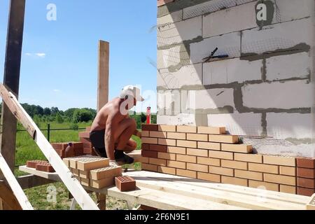 Der Meister stellt das Mauerwerk aus dem vorderen Ziegel, die Erwärmung des Hauses draußen, die Bauarbeiten im Sommer.neu Stockfoto