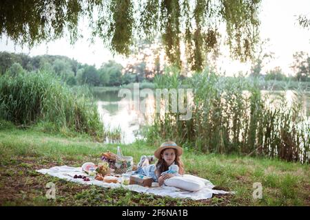 Ein Mädchen in Strohhut ist auf einem Picknick in Ein Park am Ufer eines Flusses Stockfoto