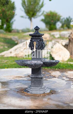 Schöner schwarzer Trinksäulenbrunnen mit Wasserhähnen auf der Straße in der antiken Touristenstadt Hierapolis, Pamukkale, Türkei. Vertikale Aufnahme. Stockfoto
