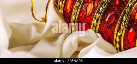 Rot glänzendes weihnachtsspielzeug liegt auf einem weißen Seidentuch. Weihnachtsschmuck und eine rote Schleife isoliert auf weiß. Hängende Kugeln, Sterne und Schneeflocken. Stockfoto