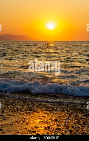 Ein farbenfroher Ocean Sunset Sky als sanfter Wave Rolls Shore in einem vertikalen Bildformat Stockfoto