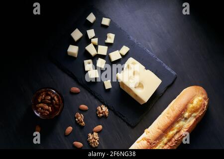 Maasdam-Käse, mit Nüssen, Honig und Baguette auf schwarzem Hintergrund. Draufsicht, Kopierbereich. Stockfoto