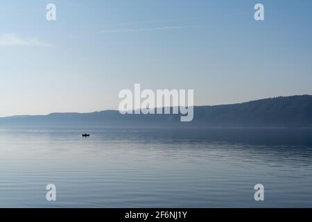 Ein Blick auf einen ruhigen blauen See mit einem kleinen Motorboot, das durch das Wasser fährt Stockfoto