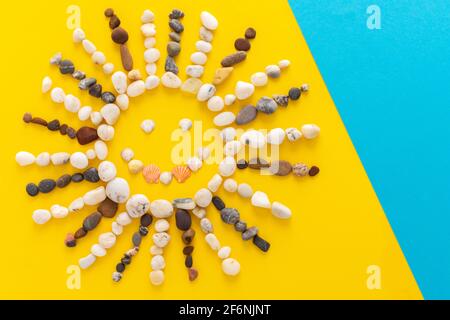 Abstrakt lächelnde Sonne aus Meereskieseln und Muscheln auf gelbem und blauem Hintergrund, Kopierraum, Urlaub am Meer oder Meer Stockfoto