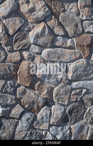 Ungerade geformte Steine oder Felsen passen zusammen wie ein Puzzle, um eine konstruierte Steinmauer Mauerwerk Haus Außenwand Hintergrund Hintergrund oder Tapete zu schaffen Stockfoto