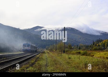 Diesel-Zug auf der Bergbahn und atemberaubende Aussicht auf Bergkette in den Wolken, Karpaten Berge, Ukraine Stockfoto