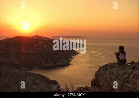 Folegandros, Griechenland - 4. August 2014 : Eine einzige Person, die auf einer Klippe sitzt und den atemberaubenden Sonnenuntergang der Folegandros kykladen in Griechenland beobachtet Stockfoto