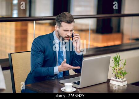 Wütend. Geschäftsmann in einem blauen Anzug, der am Telefon telefoniert und wütend aussammt Stockfoto