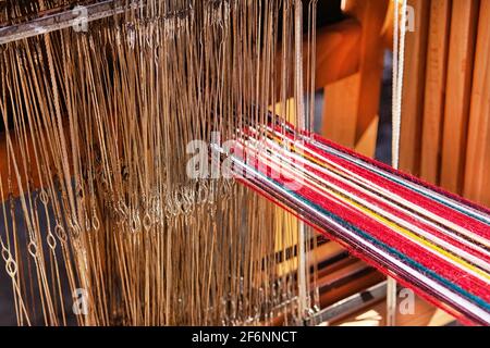 Die Strähne aus mehrfarbiger Wolle sind auf dem traditionellen Webstuhl eingefädelt. Nationales Weberei Handwerk Konzept. Stockfoto