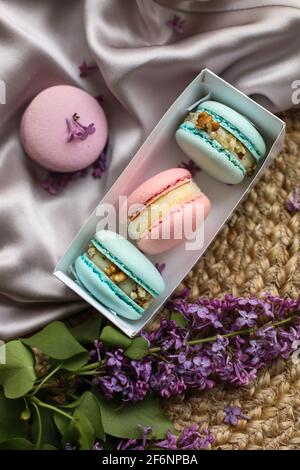 Rosa und minzfarbene französische Makronen oder Makronen-Kekse in Geschenkbox und lila Blüten auf einem Stoff- und Strohständer-Hintergrund. Natürliche Früchte und Beeren Flav Stockfoto