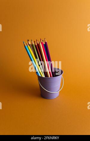 Lila Eimer mit Holzfarben auf einem dunkelorangen Hintergrund mit einem weichen Schatten. Stockfoto