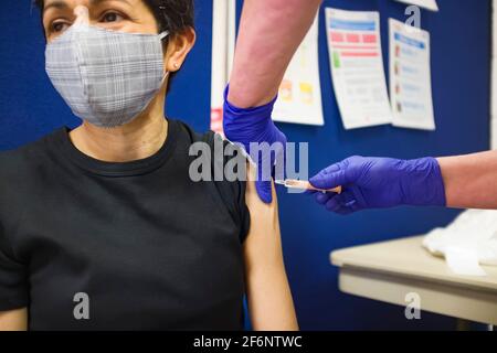 Britische Asiatin mit Gesichtsmaske, die in einem Impfzentrum in England, Großbritannien, einen Covid-19-Impfstoff erhält Stockfoto