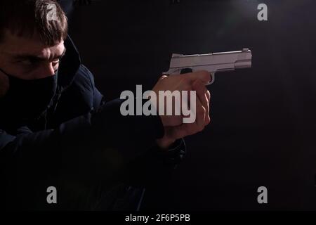 Bewaffneter Raub, Mann in Maske droht mit einer Waffe, auf schwarzem Hintergrund. Stockfoto