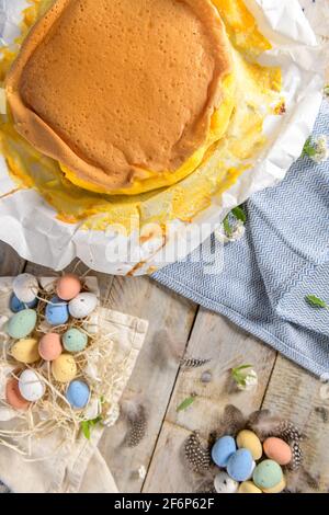 Portugiesischer Biskuitkuchen, eingewickelt in das typische Backpapier, auf Holzhintergrund mit bemaltem ostereier-Dekor. Stockfoto