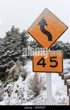 Eine kurvenreiche Straße und ein 45 km/h-Tempolimit-Schild an einem verschneiten Berghang. Mount Ruapehu, Neuseeland Stockfoto