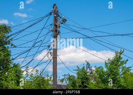 Ein alter hölzerner elektrischer Mast mit vielen Drähten gegen den blauen Himmel. Stockfoto