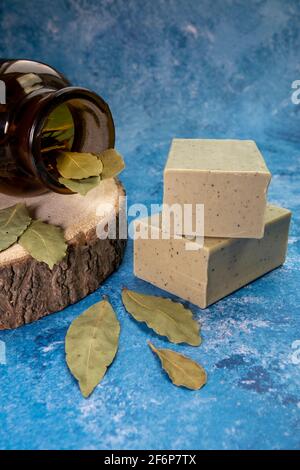 Aleppo Seife und dray Laurus nobilis Leafs in einem Holzteller und dunkle botanische Glasflasche. Stockfoto