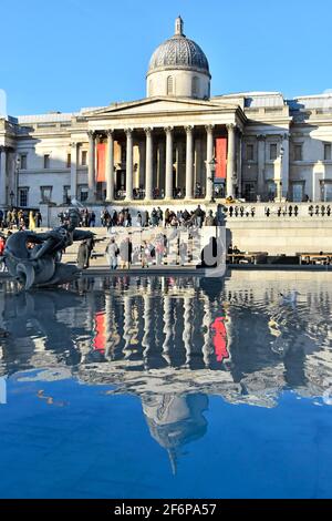 Winteransicht von Touristen & Reflexionen im Trafalgar Square Wasser Springbrunnenpool im berühmten historischen Kunstmuseum der National Gallery London, England, Großbritannien Stockfoto