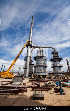 Aktau, Kasachstan - 19. Mai 2012: Bau einer asphaltischen Bitumenfabrik Raffineriesäule. Destillationsturm und gelber hydraulischer Hebezeug. Stockfoto