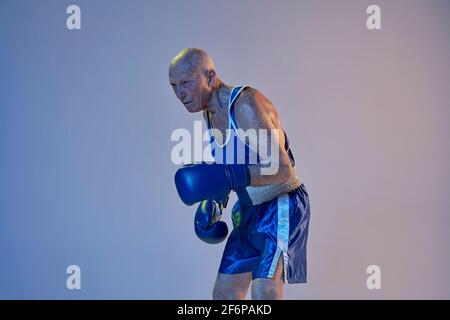 Senior Mann trägt Sportkleidung Boxen isoliert auf Gradienten Studio Hintergrund in Neonlicht. Konzept von Sport, Aktivität, Bewegung, Wohlbefinden. Copyspace Stockfoto